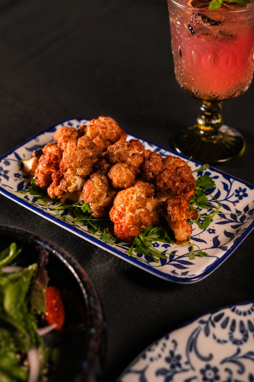 Crispy spiced cauliflower beside a jewelled cocktail glass